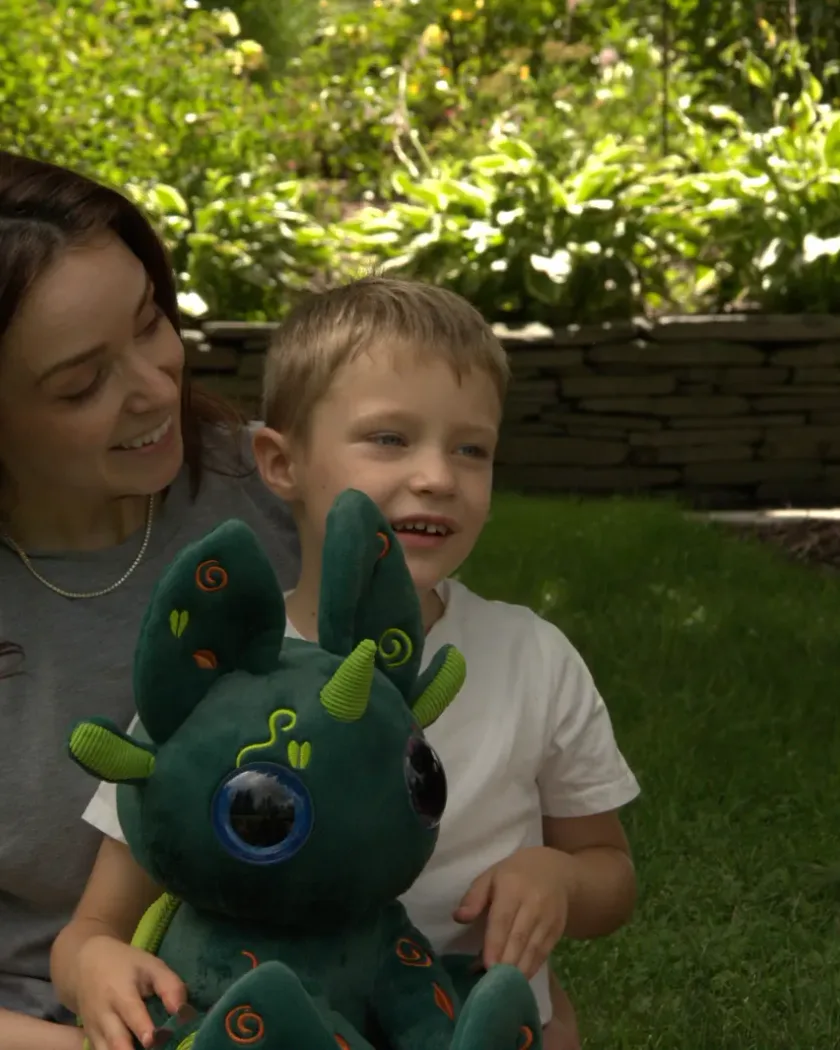 A mother and her son sitting on the grass in a garden, the boy holding a green Bloom in his lap.