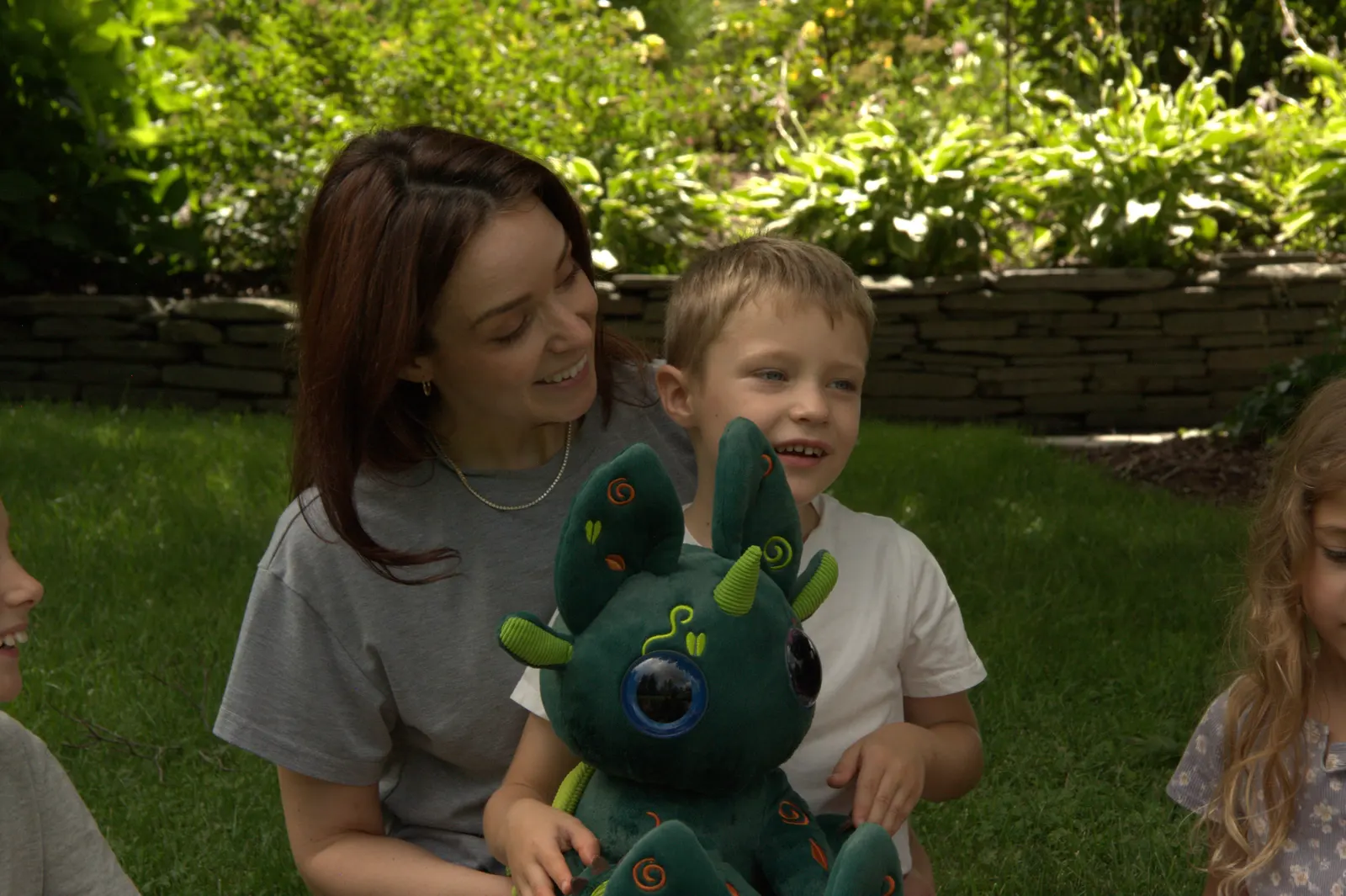A parent and two children sitting on the grass together, one child holding a green Bloom.