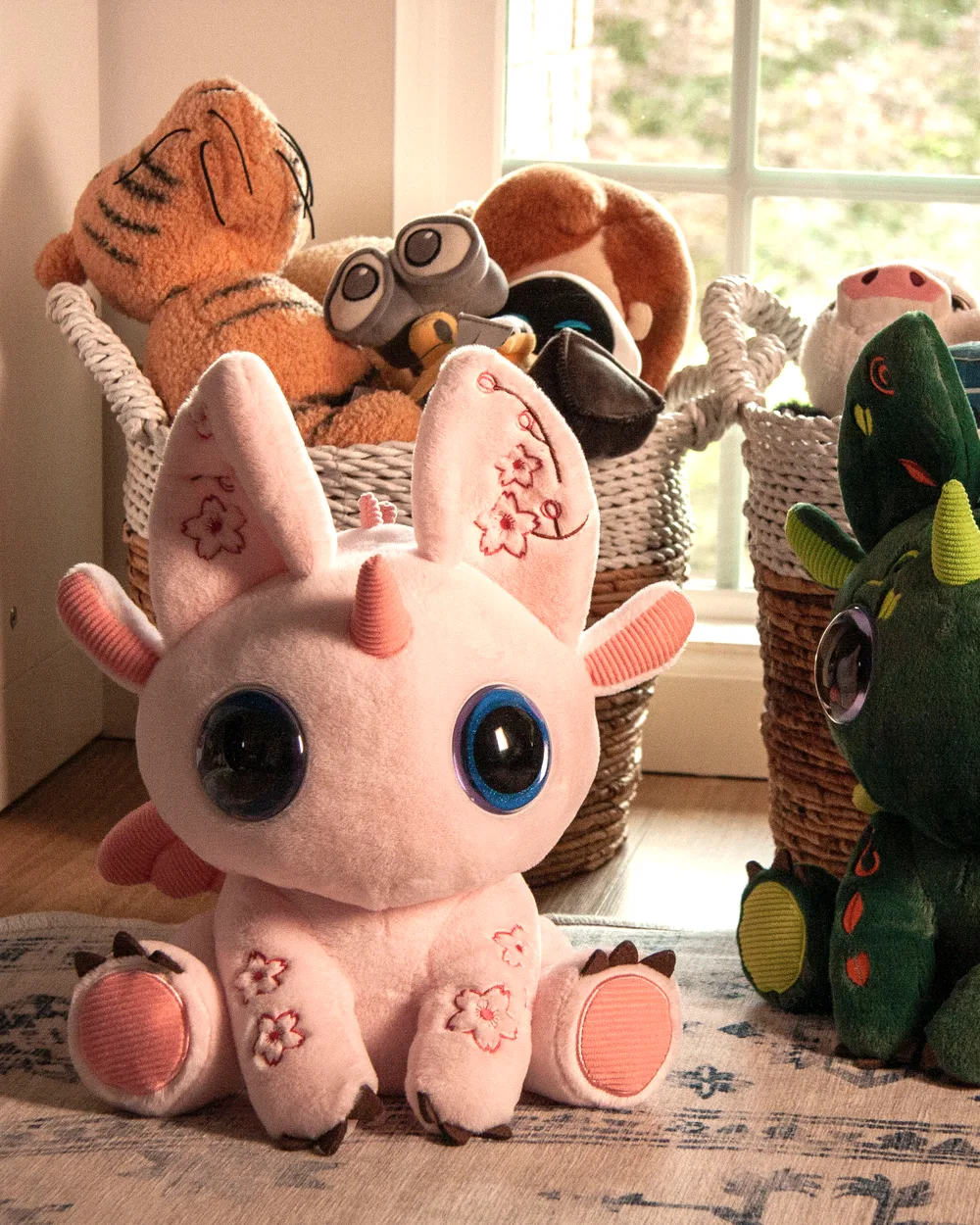 A pink and a green Bloom on a rug in a child's playroom, beside baskets of soft toys in warm window light.
