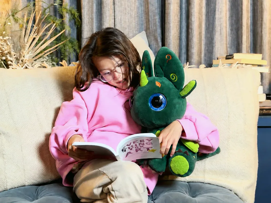 A girl in a pink hoodie reading a picture book on a sofa, with Bloom held in her lap.