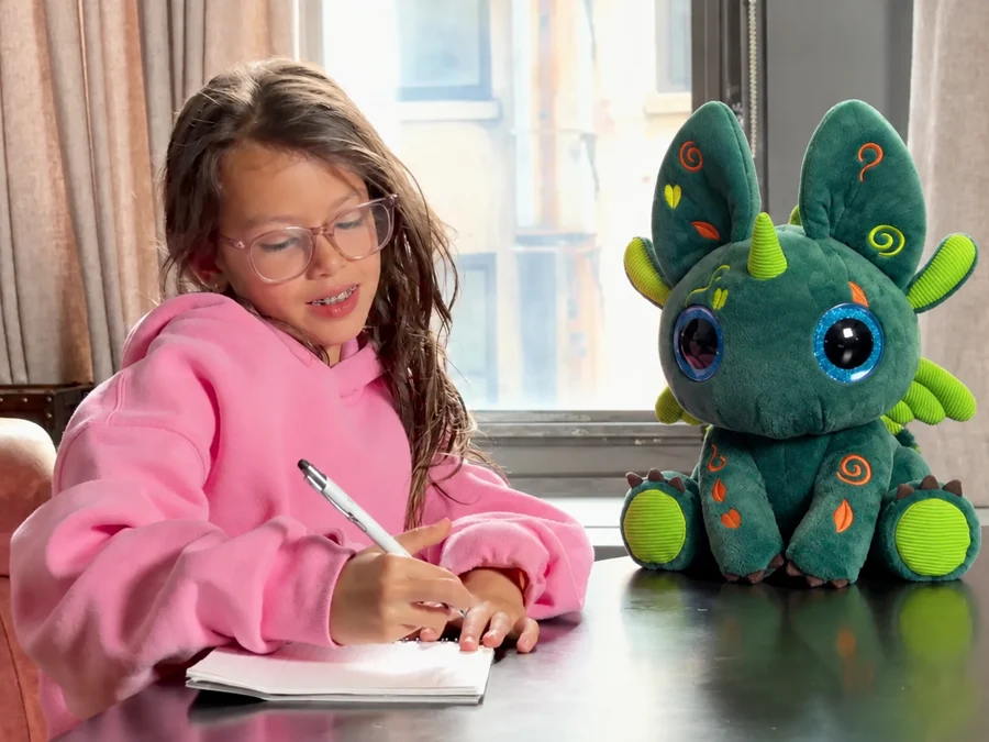A girl writing in a notebook at a table, with Bloom sitting beside her.